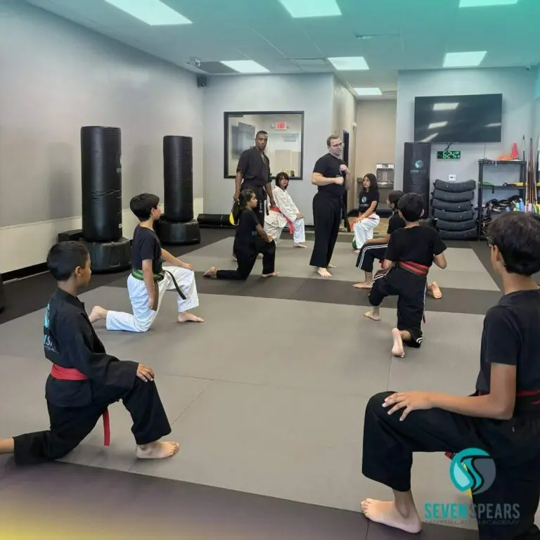 Students kneeling in a lunge stance during an instructor demonstration in a dojo martial arts classes